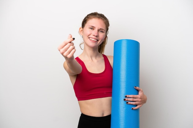 Jeune femme anglaise sportive allant à des cours de yoga tout en tenant un tapis isolé sur fond blanc faisant un geste d'argent