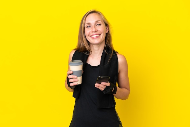 Jeune femme anglaise sportive isolée sur fond blanc tenant du café à emporter et un mobile