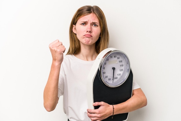 Jeune femme anglaise tenant une balance isolée sur fond blanc montrant le poing à la caméra expression faciale agressive