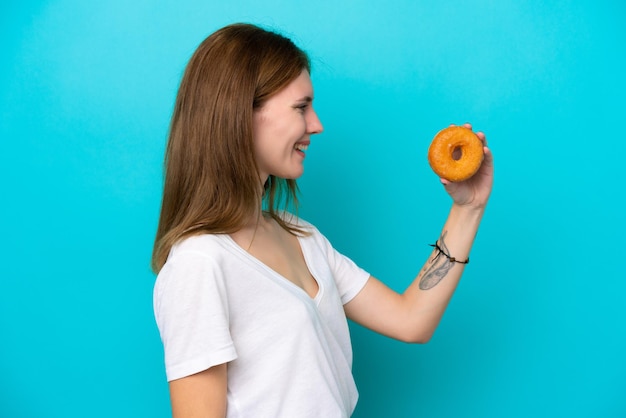 Jeune femme anglaise tenant un beignet sur fond bleu isolé avec une expression heureuse