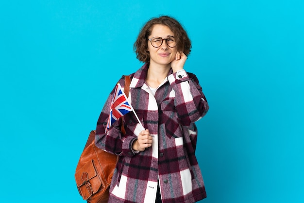 Jeune femme anglaise tenant un drapeau du Royaume-Uni sur fond bleu frustré et couvrant les oreilles