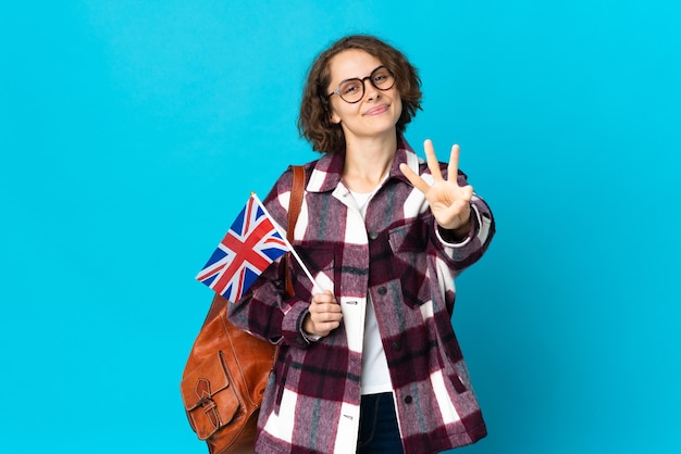 Jeune femme anglaise tenant un drapeau du Royaume-Uni isolé sur l'espace bleu heureux et en comptant trois avec les doigts