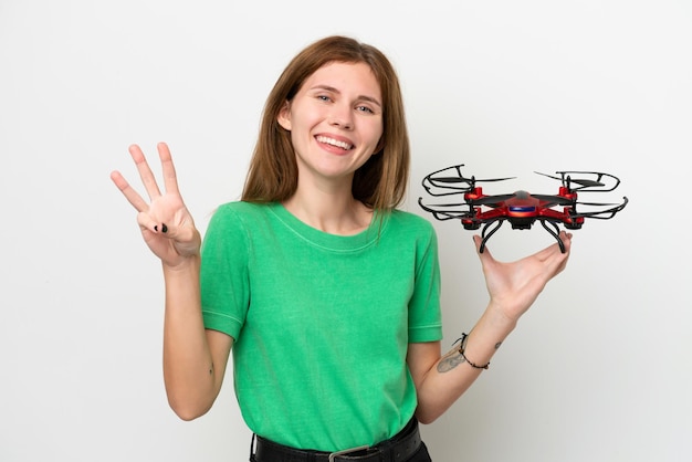 Jeune femme anglaise tenant un drone isolé sur fond blanc heureux et comptant trois avec les doigts