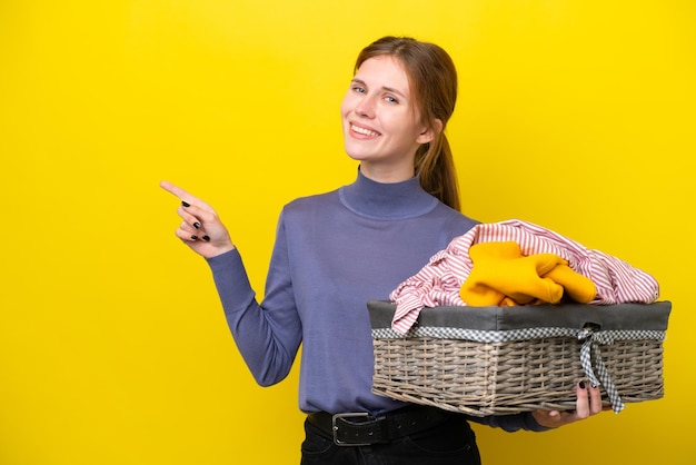 Jeune femme anglaise tenant un panier à linge isolé sur fond jaune pointant le doigt sur le côté