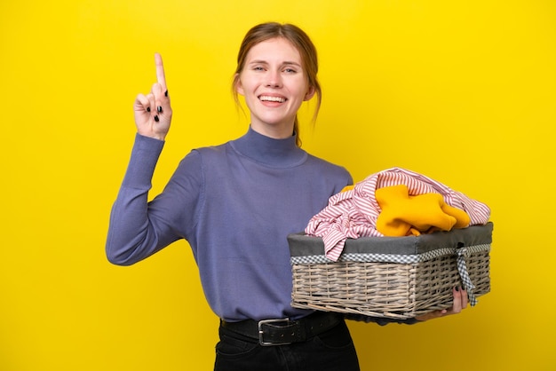 Jeune femme anglaise tenant un panier à linge isolé sur fond jaune pointant vers le haut une excellente idée