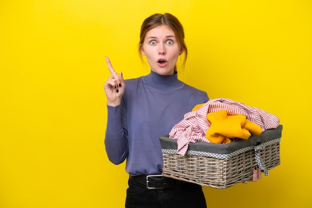 Jeune femme anglaise tenant un panier à vêtements isolé sur fond jaune dans l'intention de réaliser la solution tout en levant un doigt