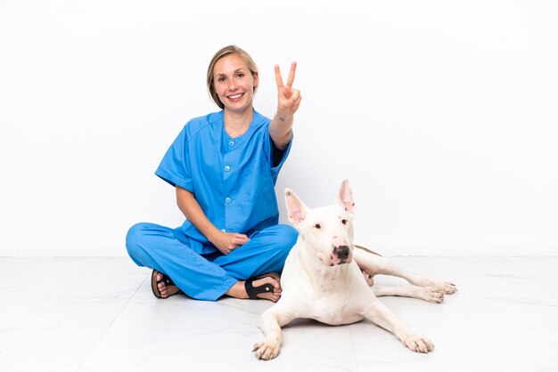 Jeune femme anglaise vétérinaire assise sur le sol avec un chien souriant et montrant le signe de la victoire