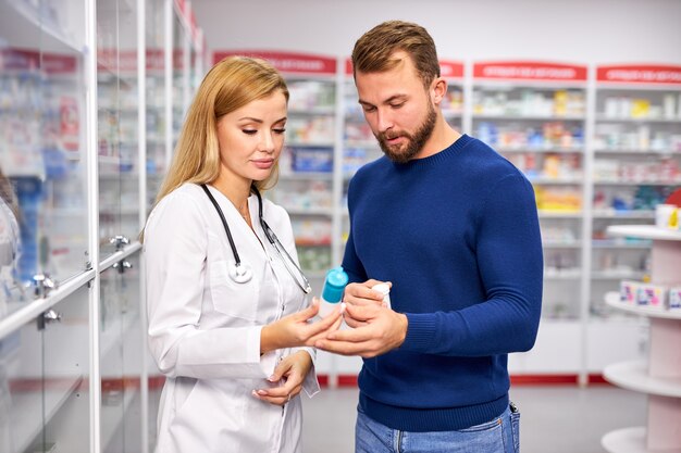 Jeune femme apothicaire avec médicament et client masculin à la pharmacie