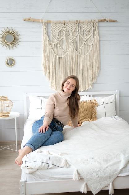 Une jeune femme d&#39;apparence européenne est assise sur le lit dans sa chambre confortable avec un sourire sur son visage