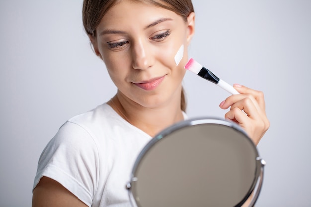 Jeune femme appliquant une crème hydratante sur son visage devant le miroir