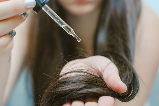 Jeune femme appliquant de l&#39;huile sur ses cheveux, à l&#39;intérieur