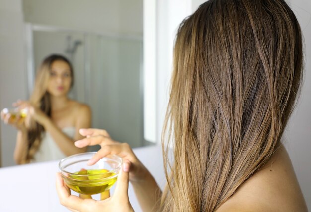 Jeune femme appliquant un masque à l'huile d'olive sur les cheveux devant un miroir