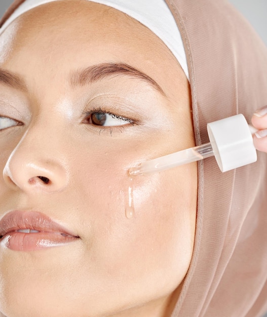 Photo une jeune femme appliquant un sérum facial anti-âge sur son visage et sa peau belle fille musulmane portant un hijab essayant du rétinol avec un compte-gouttes comme routine de soins de la peau et régime de soins de beauté