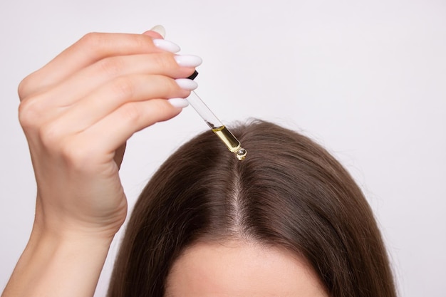 Une jeune femme applique une goutte d'huile d'une pipette sur son cuir chevelu.