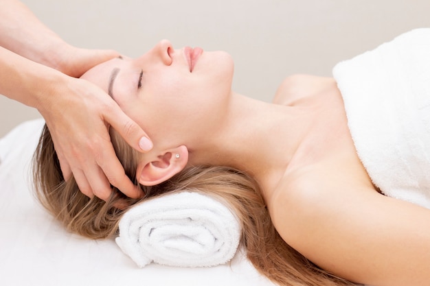 Jeune femme appréciant le massage dans le salon spa. Massage du visage. Gros plan de jeune femme recevant un traitement de massage spa au salon de beauté spa.Spa et soins du corps. Traitement de beauté du visage Cosmétologie.