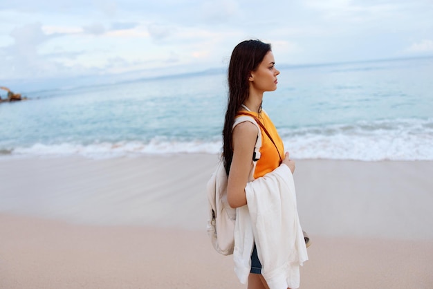 Une jeune femme après avoir nagé dans l'océan avec un sac à dos dans des vêtements mouillés se promène le long des vacances d'été à la plage sur une île près de l'océan à Bali