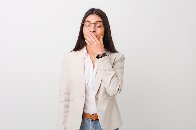 Jeune femme arabe d'affaires isolée contre un mur blanc bâillant montrant un geste fatigué couvrant la bouche avec la main.