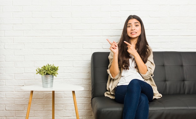 Jeune femme arabe assise sur le canapé, choquée, pointant du doigt l'index d'une copie.