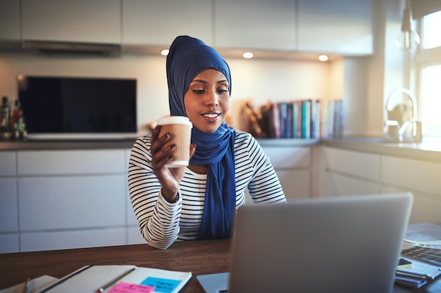 Une jeune femme arabe buvant du café et travaillant en ligne à la maison