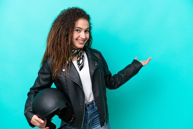 Jeune femme arabe avec un casque de moto isolé sur fond bleu tendant les mains sur le côté pour inviter à venir