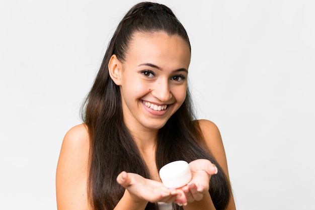 Jeune femme arabe sur fond blanc isolé avec crème hydratante et l'offrant