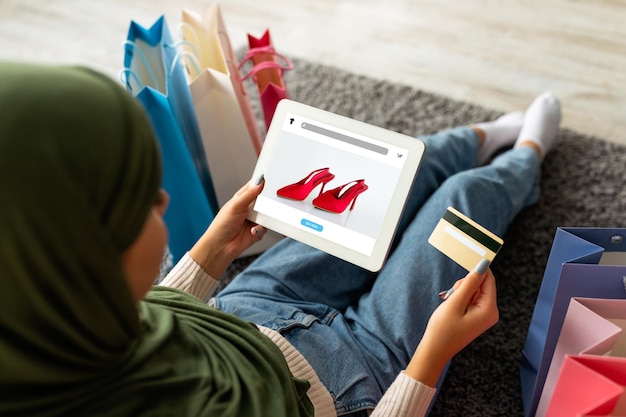 Photo jeune femme arabe en hijab utilisant une carte de crédit et une tablette avec un magasin de mode à l'écran offrant un site web