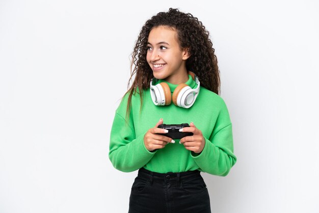 Jeune femme arabe jouant avec un contrôleur de jeu vidéo isolé sur fond blanc regardant sur le côté et souriant