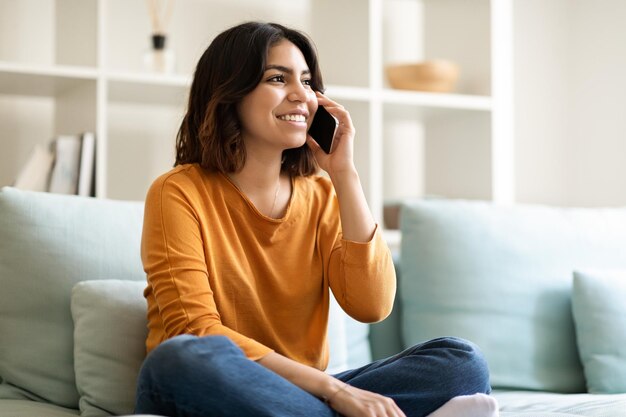 Jeune femme arabe parlant sur téléphone portable et se détendre sur un canapé à la maison