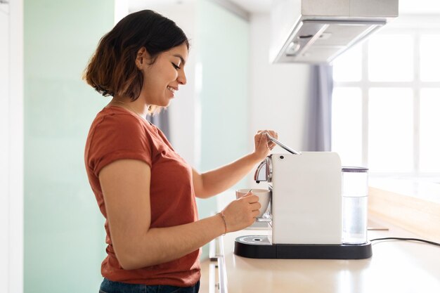 Jeune femme arabe souriante préparant du café frais avec une machine moderne dans la cuisine