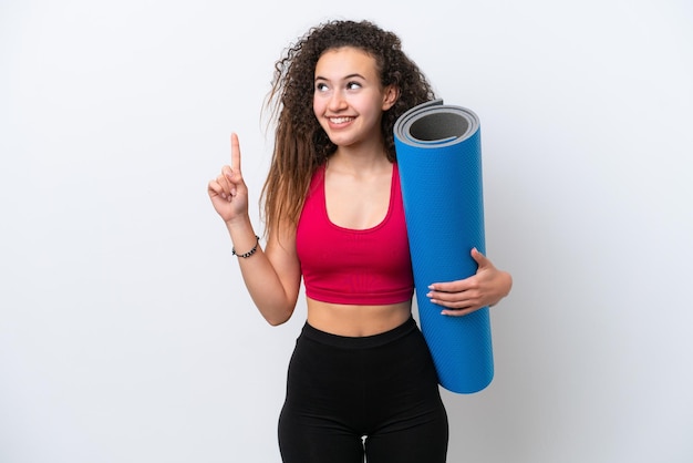 Jeune femme arabe sportive allant à des cours de yoga tout en tenant un tapis isolé sur fond blanc pointant vers le haut une excellente idée