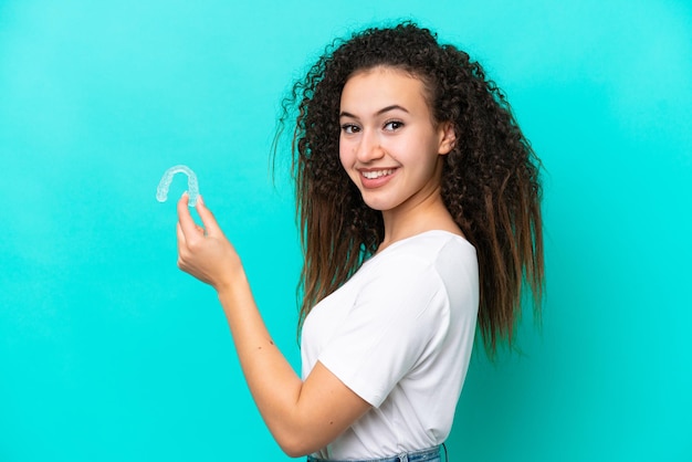 Jeune femme arabe tenant des bretelles invisibles isolées sur fond bleu souriant beaucoup