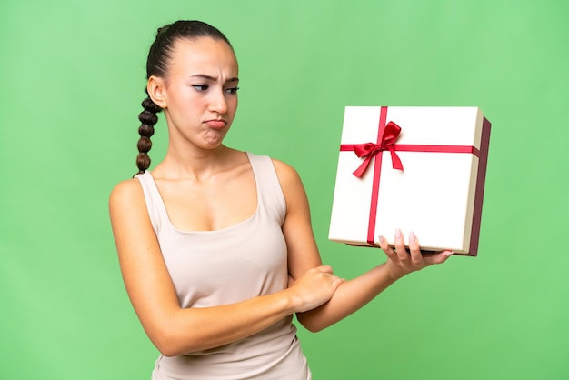 Jeune femme arabe tenant un cadeau sur fond isolé avec une expression triste