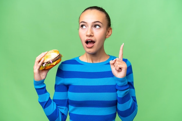 Jeune femme arabe tenant un hamburger sur fond isolé en pensant à une idée pointant le doigt vers le haut