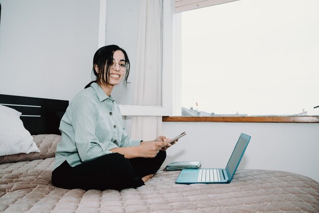 Jeune femme arabe travaillant à la maison sur son ordinateur portable tout en utilisant son téléphone