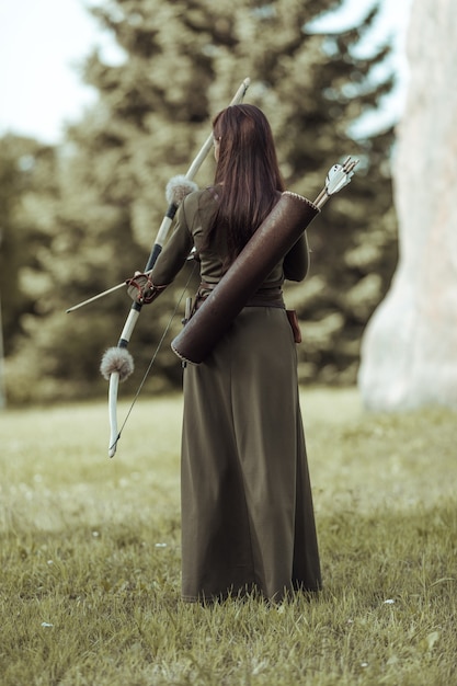 Jeune femme archer en costume médiéval vert se dresse avec son dos