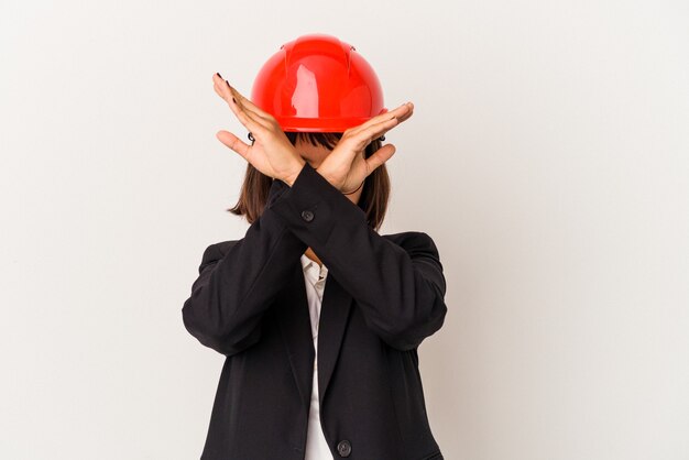 Jeune femme architecte avec casque rouge isolé sur fond blanc en gardant les deux bras croisés, concept de déni.