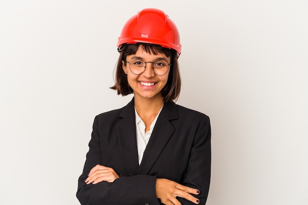 Jeune femme architecte avec casque rouge isolée sur fond blanc qui se sent confiante, croisant les bras avec détermination.