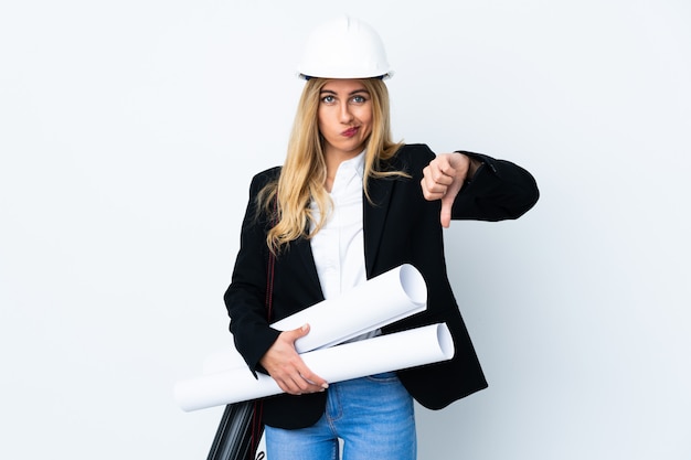 Jeune femme architecte avec casque et tenant des plans sur blanc isolé montrant le signe du pouce vers le bas