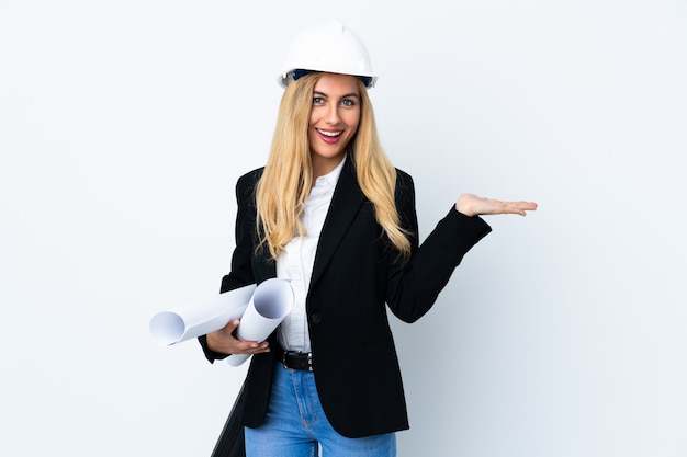 Jeune femme architecte avec casque et tenant des plans sur fond blanc isolé copyspace holding imaginaire sur la paume