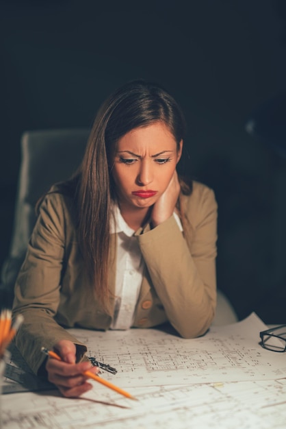 Jeune femme architecte inquiète analysant le plan au bureau.