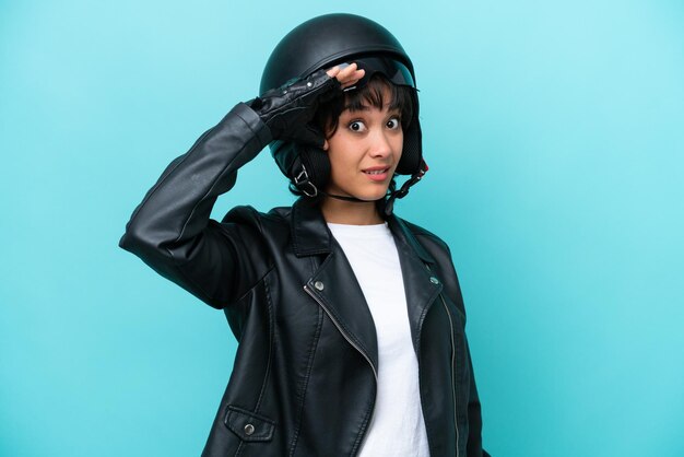 Jeune femme argentine avec un casque de moto isolé sur fond bleu faisant un geste de surprise tout en regardant sur le côté