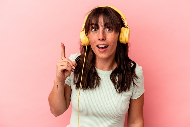 Jeune femme argentine écoutant de la musique isolée sur fond rose ayant une idée, un concept d'inspiration.