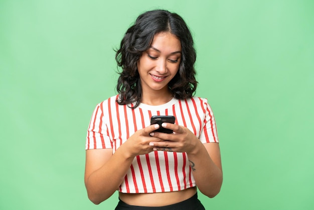 Jeune femme argentine sur fond isolé envoyant un message avec le mobile