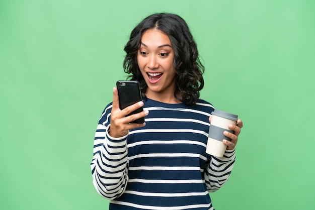 Jeune femme argentine sur fond isolé tenant du café à emporter et un mobile