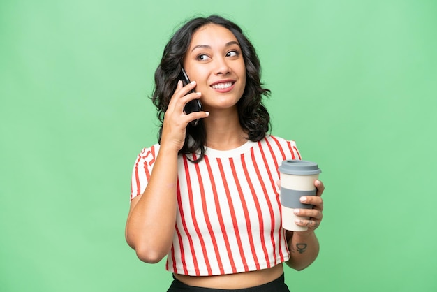 Jeune femme argentine sur fond isolé tenant du café à emporter et un mobile