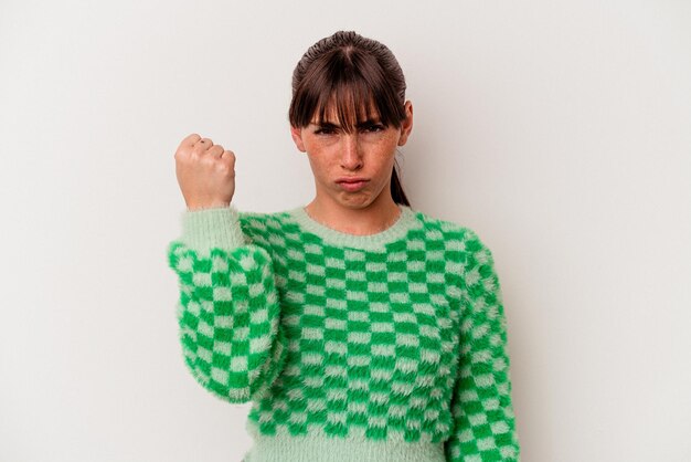 Jeune femme argentine isolée sur fond blanc montrant le poing à la caméra, expression faciale agressive.