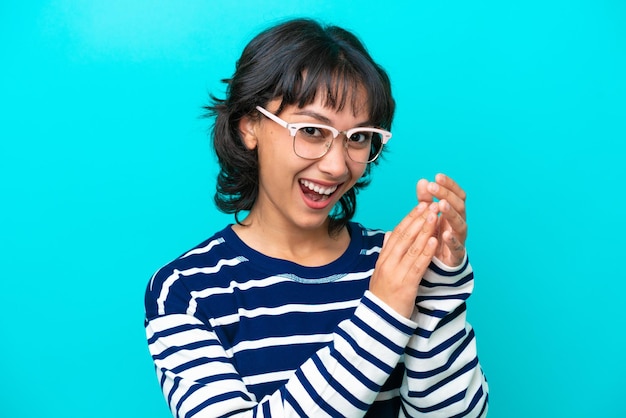 Jeune femme argentine isolée sur fond bleu avec des lunettes et applaudissant