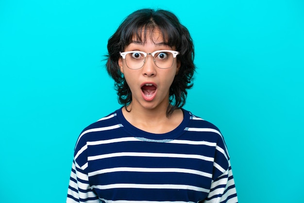 Jeune femme argentine isolée sur fond bleu avec des lunettes et une expression surprise