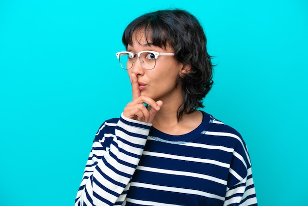 Jeune femme argentine isolée sur fond bleu avec des lunettes et faisant un geste de silence