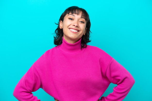 Jeune femme argentine isolée sur fond bleu posant avec les bras à la hanche et souriant